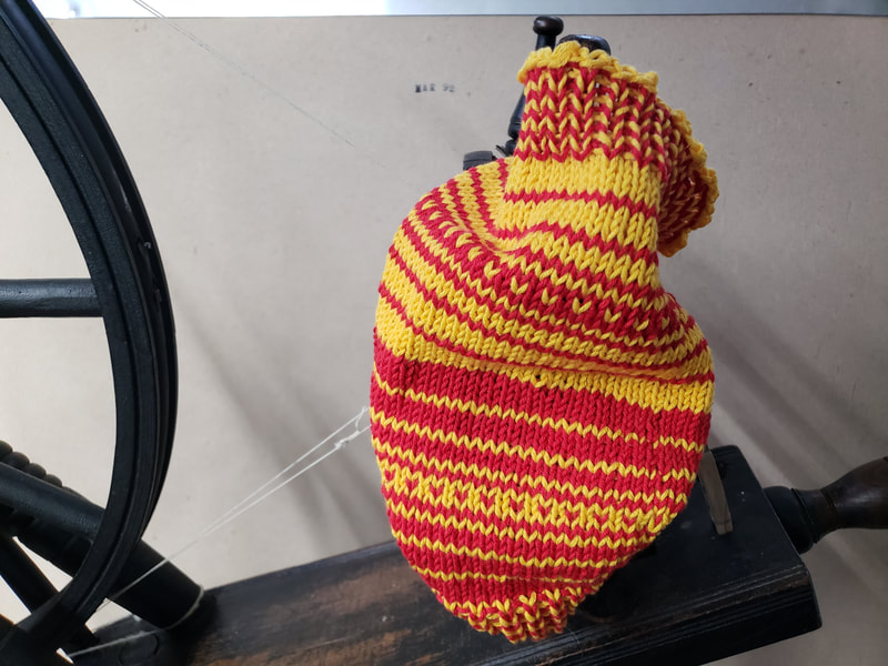 A red and yellow knit cowl displayed on a spinning wheel. 