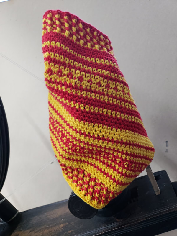A red and yellow crochet cowl displayed on a spinning wheel.