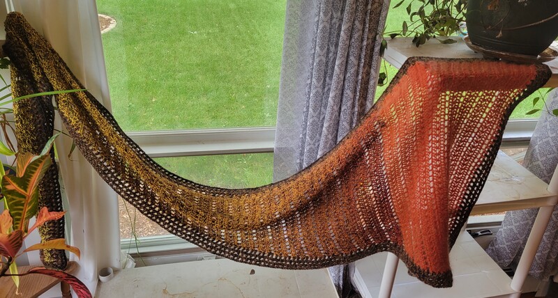 A red and  yellow crochet scarf draped across a window