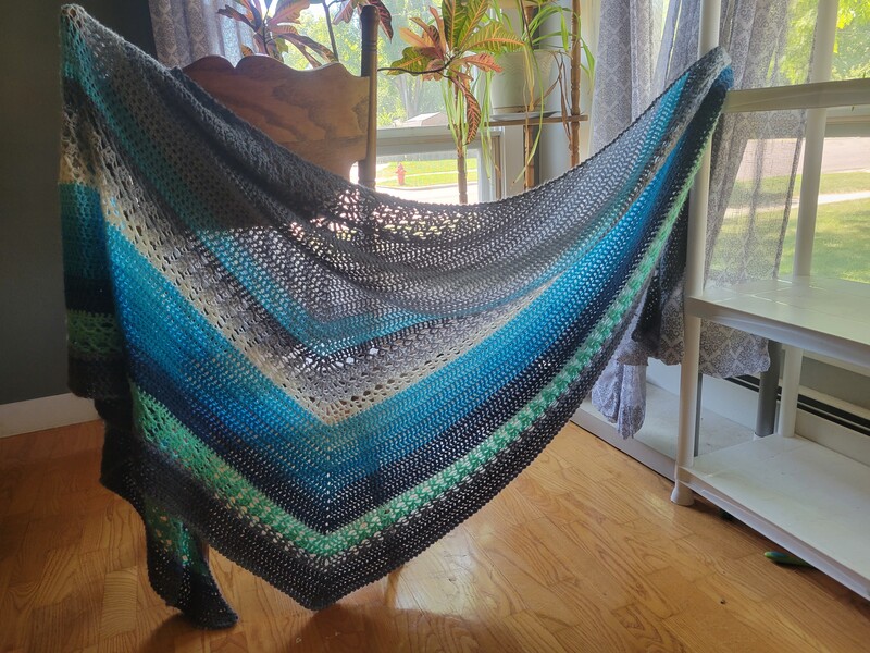 Blue, green, and gray shawl draped across a plant filled window