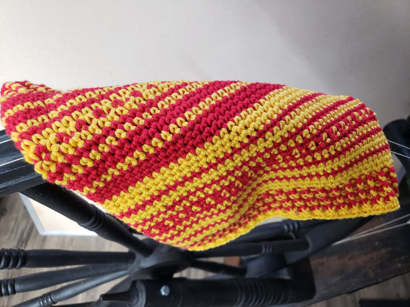 A red and yellow cowl draped across the wheel of a spinning wheel. 