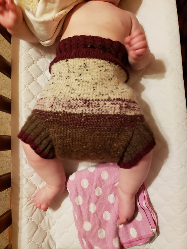 Baby on a changing table wearing a handknitted maroon, tan, and brown knit wool soaker